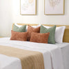 A collection of square decorative cushion covers in shades of green, brown, and white on a bed