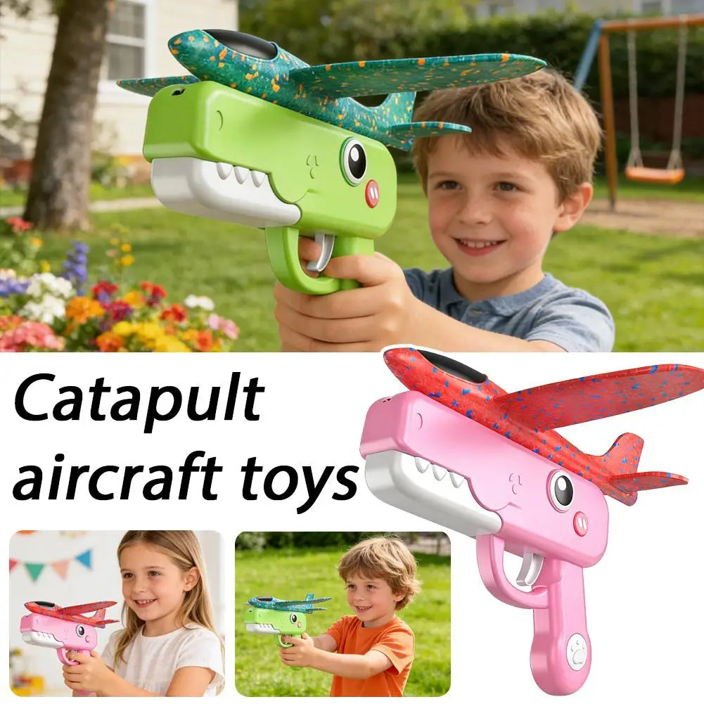 A young boy holds a pink foam catapult airplane toy with green and blue wings in an outdoor setting.