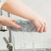 A hand is holding a gray microfiber cleaning cloth under running water.