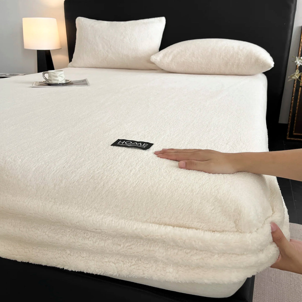A white plush mattress cover is displayed on a bed, with a hand touching the fabric.