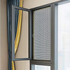 A close-up view of a dark gray mesh screen installed in a window frame with yellow curtains visible.