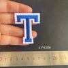 A hand holds a blue embroidered letter T patch, measuring 5.1 x 4.2 cm against a ruler.