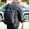 Ein Mann mit schwarzem Lederrucksack und Jeansjacke steht neben einem dunklen SUV.