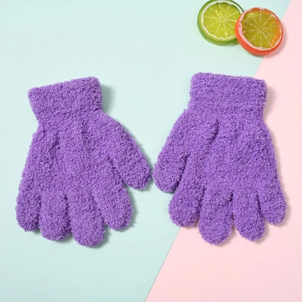A pair of purple plush winter gloves for kids resting on a light pink and mint green background with a lime slice.