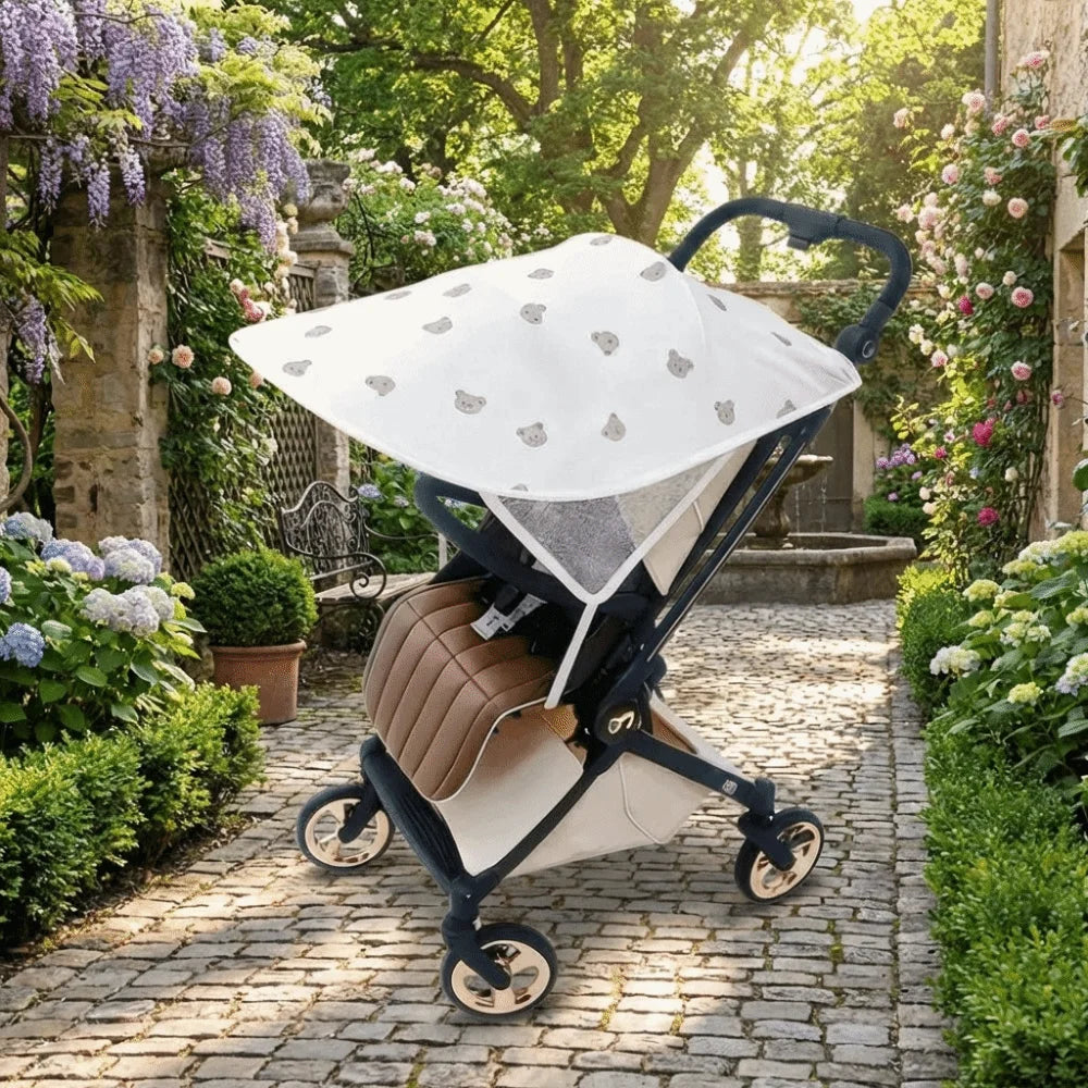 A beige and white stretchable UV-protective stroller sun shade is shown in a garden setting.