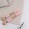 A string of pink silicone pacifier clips with baby names attached to a beige linen fabric.
