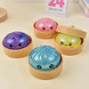 A collection of four glitter dumpling squeeze toys in pink, yellow, purple, and blue are displayed in light brown containers.