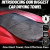 A close-up of a large black microfiber car drying towel being used on a red car surface.