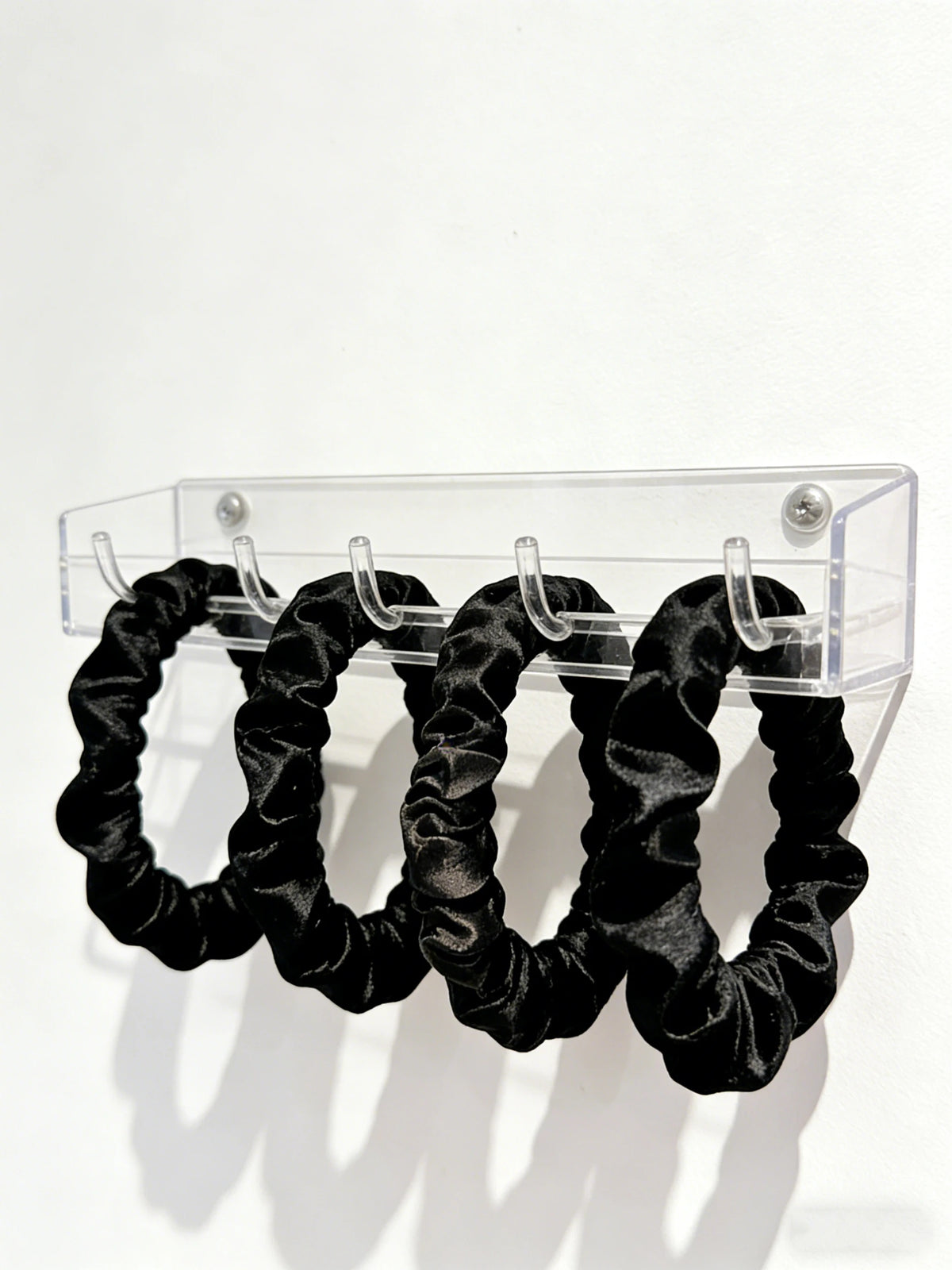 Scrunchies en satin noir skinny exposés sur un présentoir en acrylique transparent.