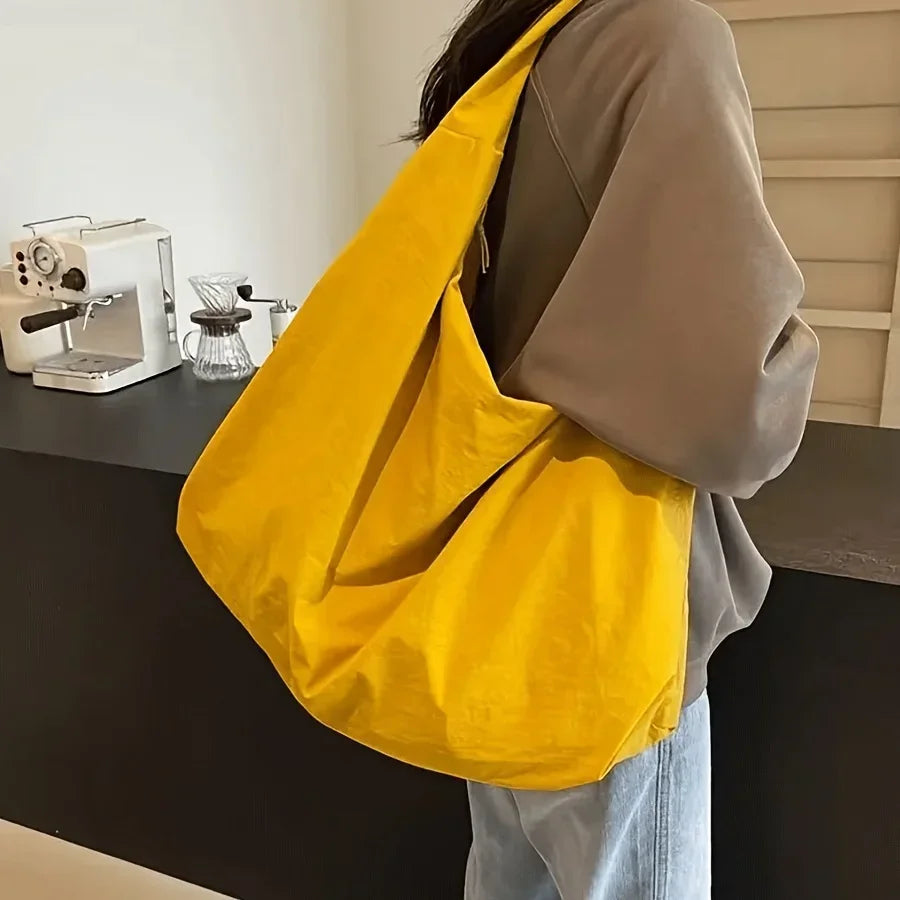 A bright yellow lightweight nylon tote bag is carried by a person wearing a gray hoodie, set against a dark surface.