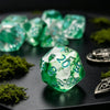 A close-up of seven fresh green polyhedral gaming dice resting on a dark surface with moss.