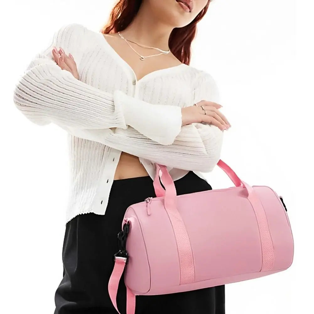 A woman holds a pink compact nylon gym bag with an adjustable strap.