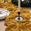 A yellow crinkle gauze cheesecloth table runner draped across a wooden surface with a white candle and green wreath.