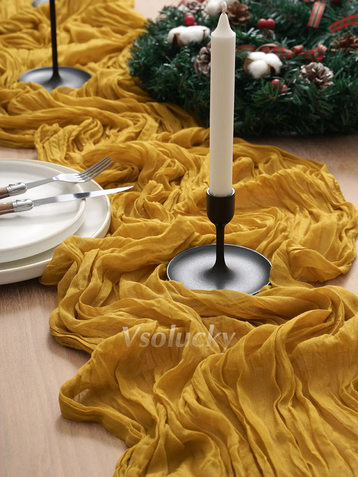 A yellow crinkle gauze cheesecloth table runner draped across a wooden surface with a white candle and green wreath.