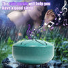 A teal steel tongue drum resting on a wet rock, with rain falling and a woman meditating nearby.