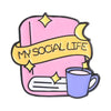 Enamel pin featuring a pink book with a yellow ribbon and a purple mug, titled My Social Life.