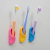 A collection of colorful adhesive wall-mounted toothbrush holders with drainage holes in pink, yellow, blue, and purple.