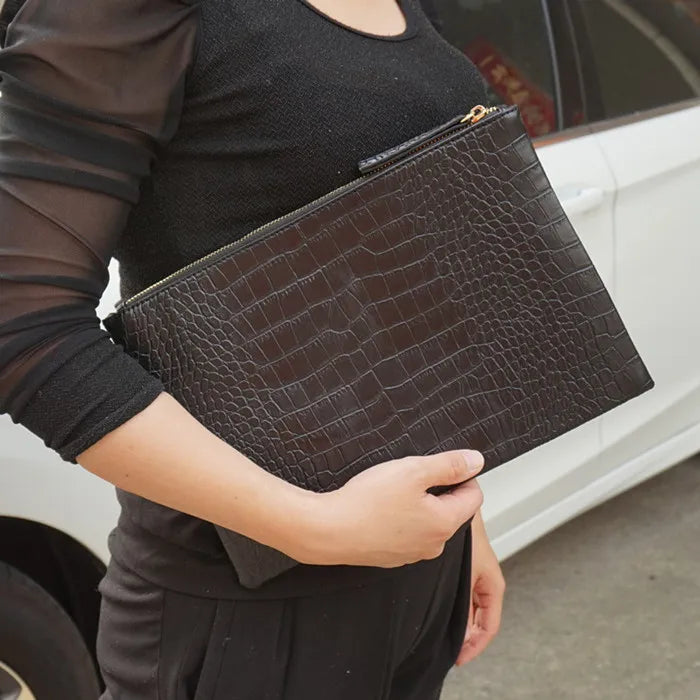 A person holding a dark brown crocodile-embossed PU leather envelope clutch against a white car.