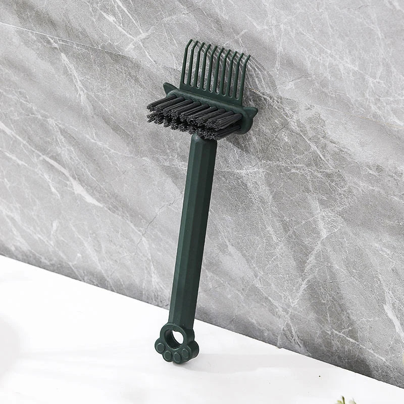 A dark green dual-sided hairbrush cleaner with rake teeth resting on a gray marble surface.