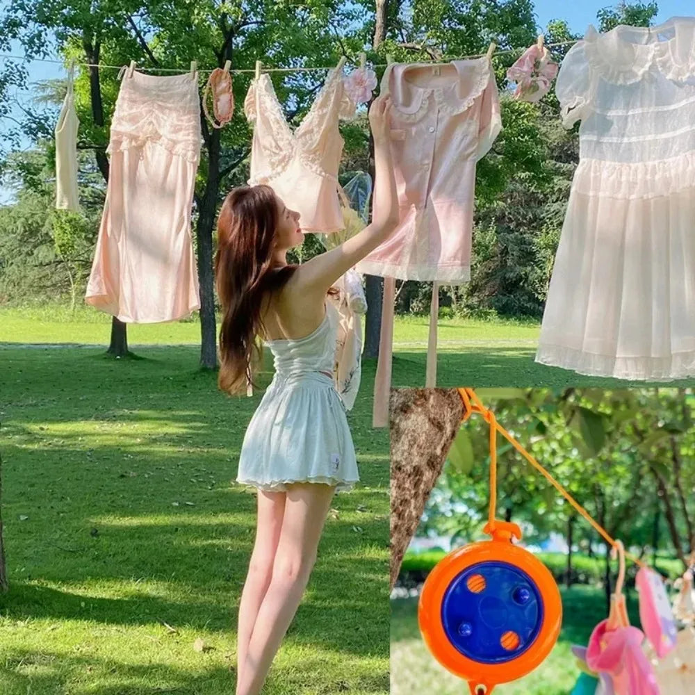 A woman is hanging light pink and white sheer clothing on a portable clothesline outdoors.