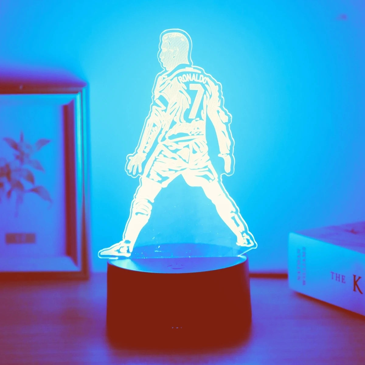 Leuchtende Silhouette eines Fußballspielers mit der Nummer 7 beleuchtet eine dunkle Fläche vor blauem Hintergrund.