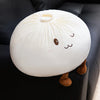Un coussin en peluche rond blanc en forme de dumpling mignon avec de petits yeux et oreilles brunes.