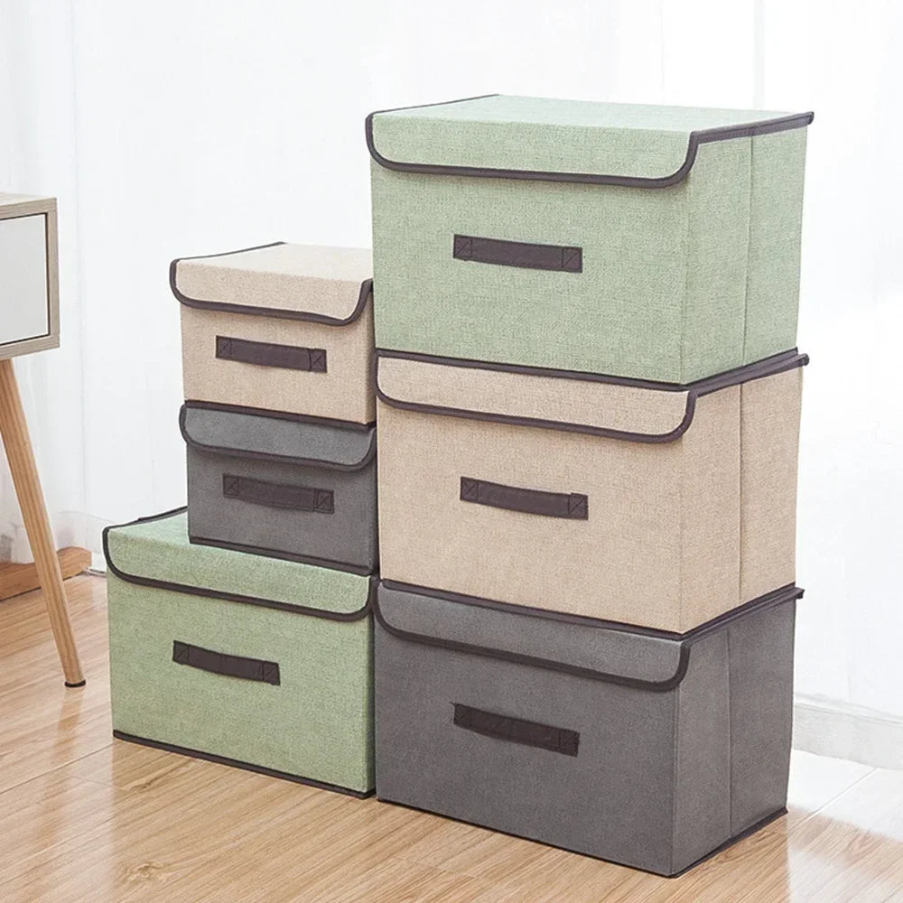 A set of four fabric storage boxes in sage green and gray are arranged on a wooden floor.