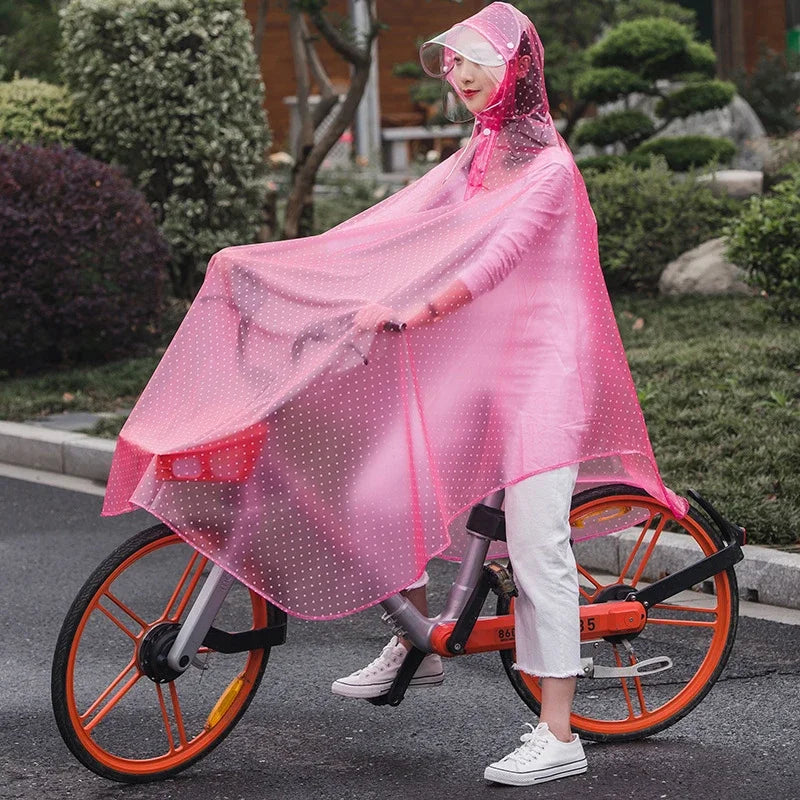 A woman wearing a sheer pink waterproof poncho with a hood rides an orange bicycle outdoors.