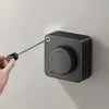A hand is activating a retractable clothesline with hidden storage mounted on a wall.