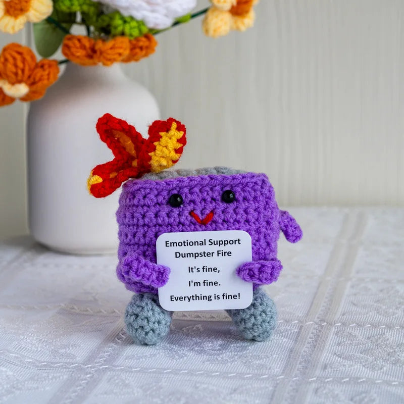 Handmade crochet dumpster fire doll with purple body and orange ears sitting on a white surface.