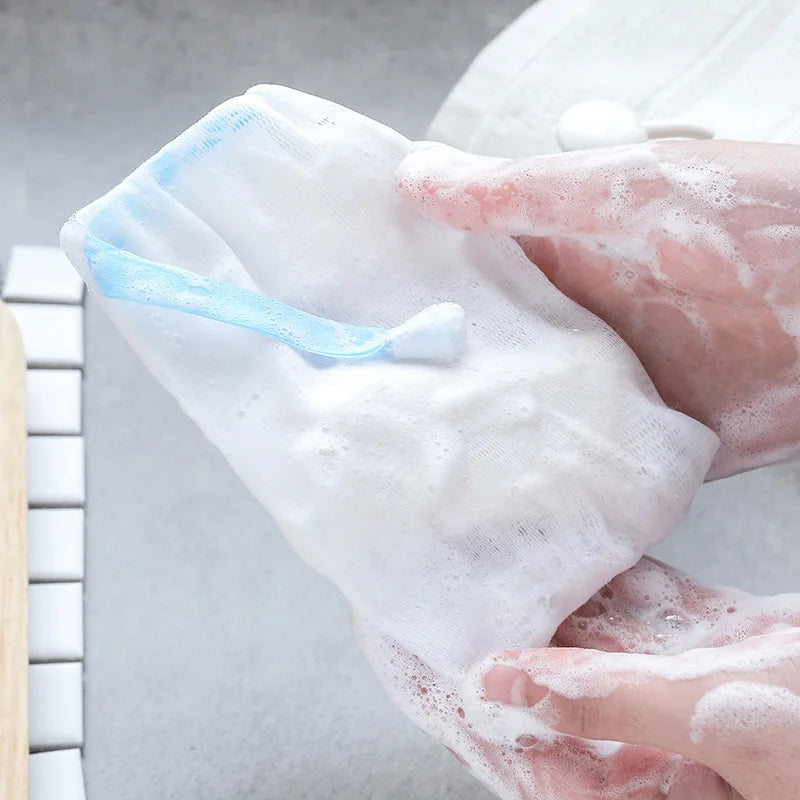 Hands are squeezing a white foaming mesh bath pouf with a blue hanging loop.