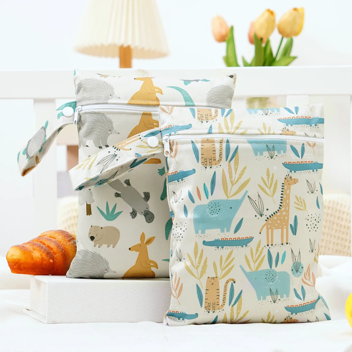 A pair of light-colored waterproof wet dry bags featuring animal designs like elephants and giraffes, resting on a white surf
