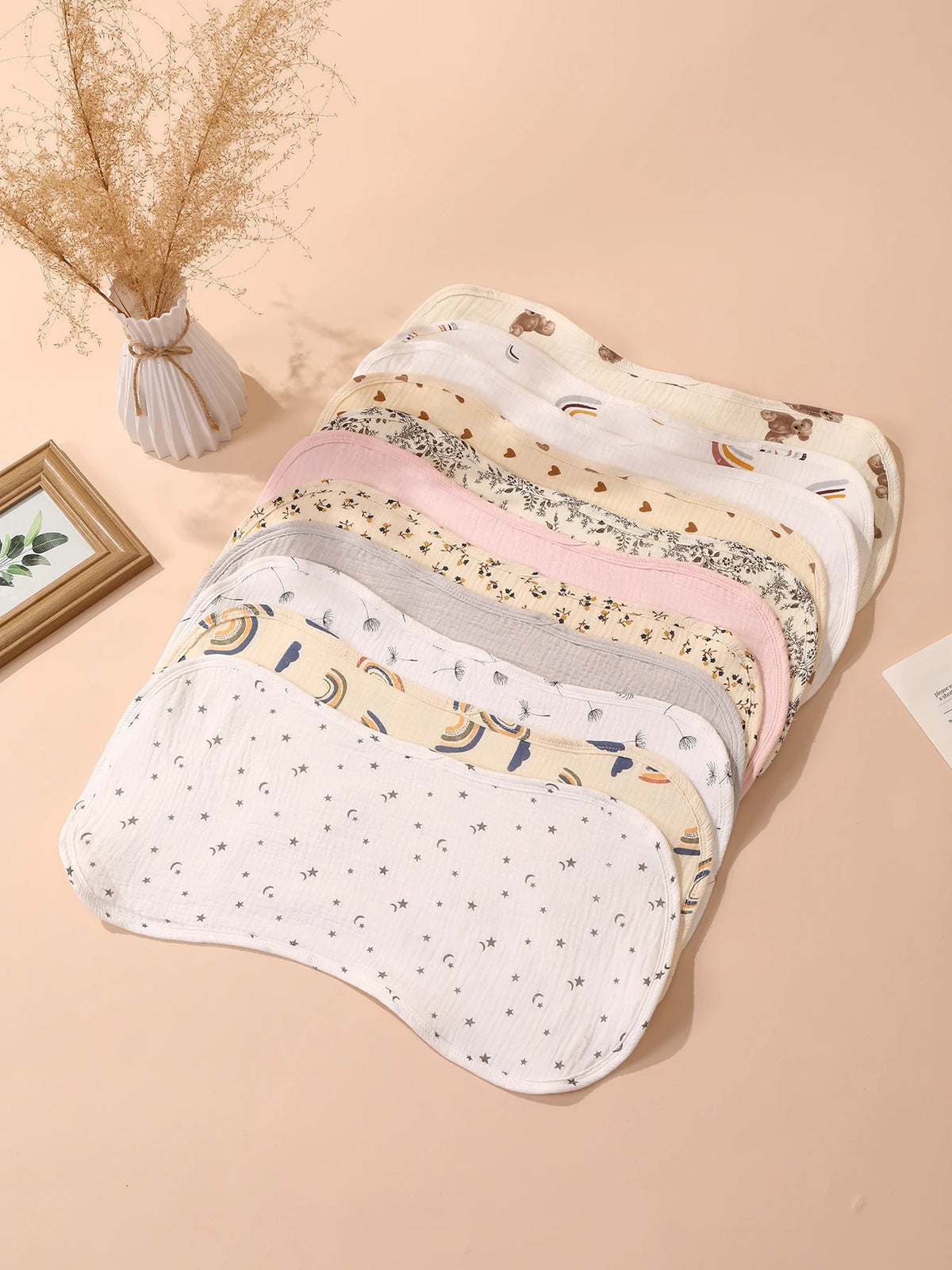 A stack of six layers of soft absorbent baby burp cloths in various pastel colors and patterns is displayed on a light backgr