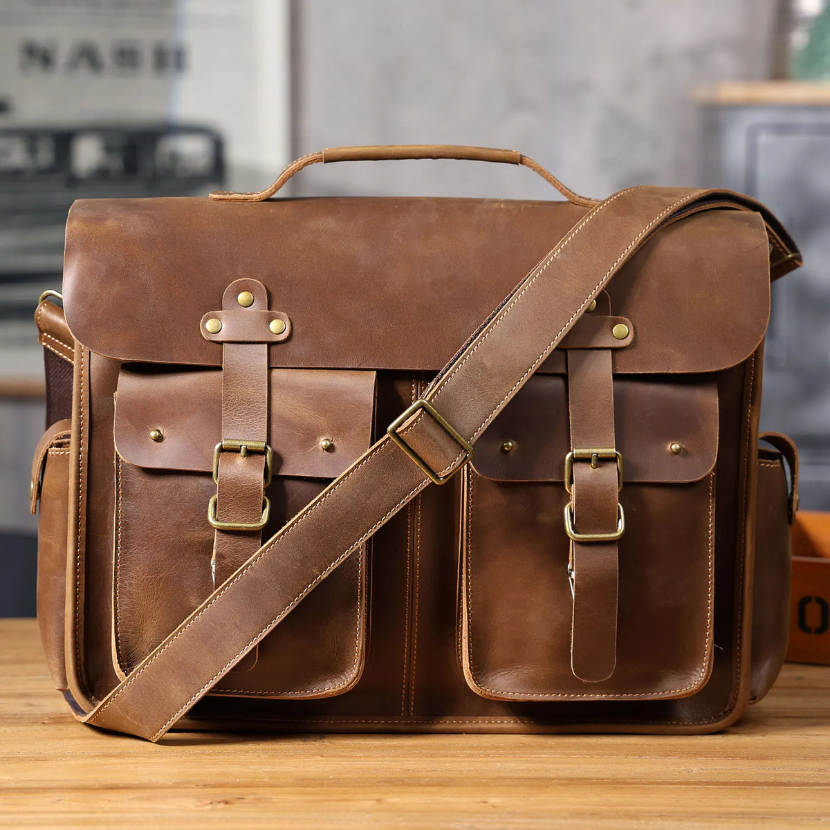 Braunes Vintage-Ledertasche mit Lederriemen und mehreren Fächern auf Holzoberfläche.