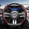 Close-up view of a black steering wheel with red carbon fiber texture accents and Mercedes-Benz instrument cluster.