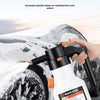A hand is using a white electric foam sprayer to wash snow off a car tire in an outdoor setting.