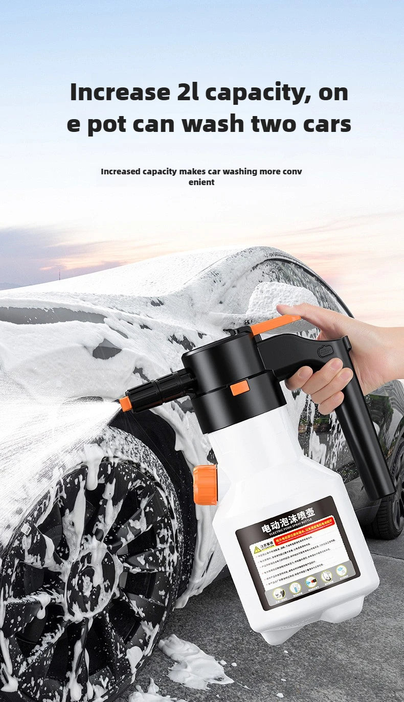 A hand is using a white electric foam sprayer to wash snow off a car tire in an outdoor setting.