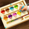 A hand is sorting colorful magnetic wooden cups into corresponding colored slots on a light wood maze board.