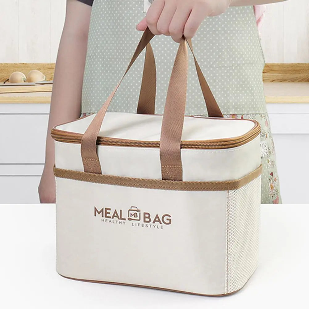 A beige insulated lunch bag with brown straps is held by a person, resting on a white surface.
