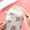 A hand holds a beige cosmetic storage pouch with green leaf embroidery and a white card inside.