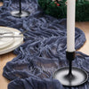 A dark blue crinkle gauze cheesecloth table runner draped over a wooden surface with a white candle and silver cutlery.