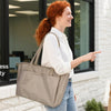 Two women are shown using a beige and black laptop tote bag in a modern office setting.