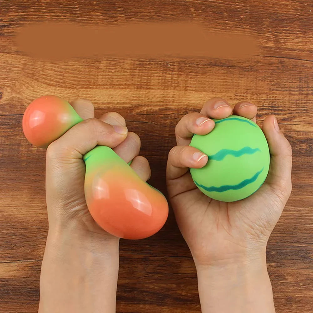 Hände halten zwei wassermelonenfarbene Stressball-Spielzeuge auf einer Holzoberfläche.