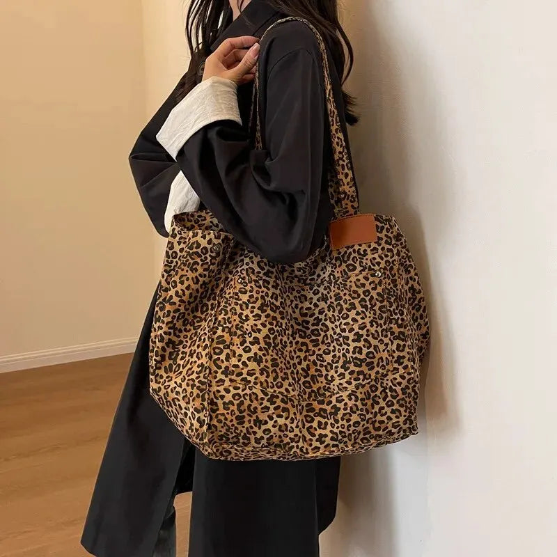A person is holding a vintage leopard print canvas tote bag with a brown leather accent against a light wall.