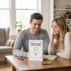 A couple looking at a personalized fill-in-the-blank love book for an anniversary keepsake journal on a wooden table.