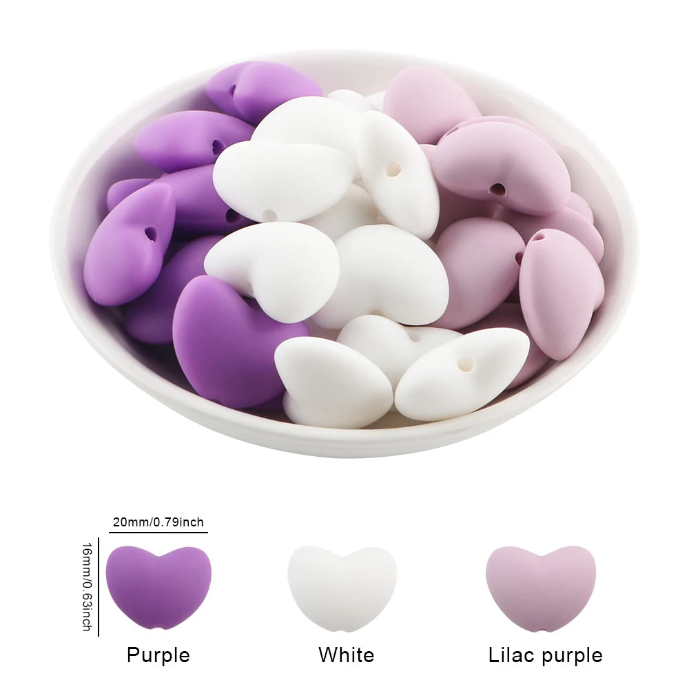 A bowl filled with ten silicone heart beads in purple, white, and lilac purple colors.