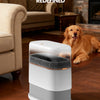 A white touchless trash can with a dark lid sits on a wooden floor next to a golden retriever.