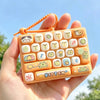 An orange cartoon keycap fidget keychain is held in a hand against a bright blue sky.