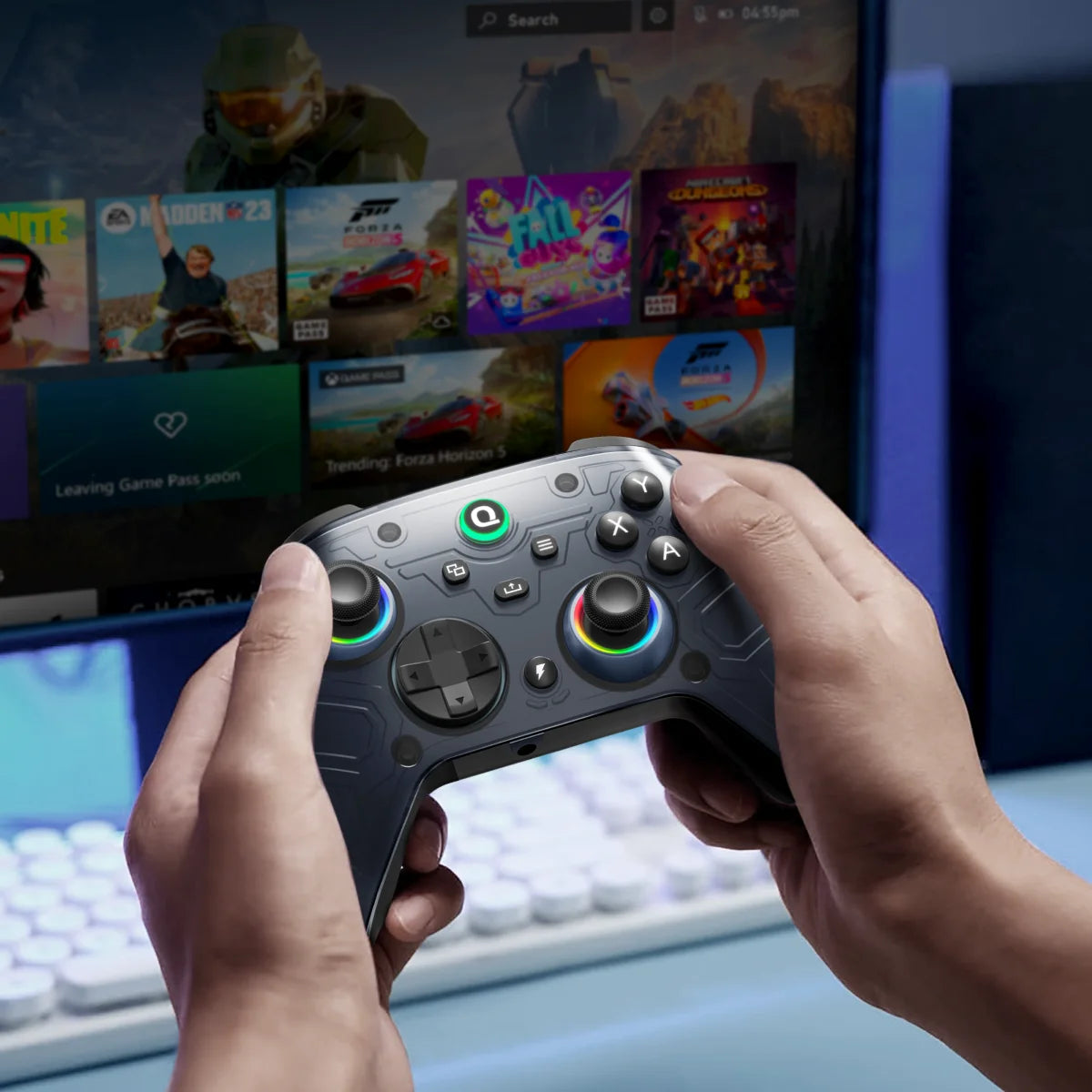 Eine Person hält einen grauen kabellosen Gaming-Controller vor einem Computerbildschirm mit Spielgrafiken.