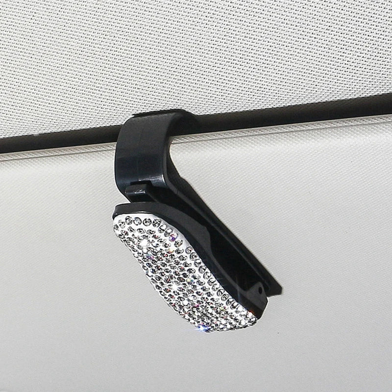 A black clip with a crystal rhinestone lens is shown against a light-colored surface.